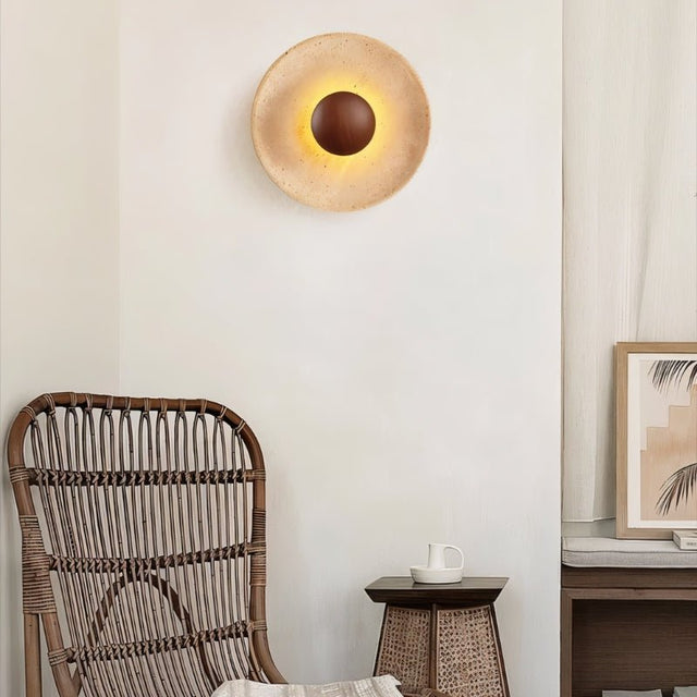 "A modern, circular wall lamp made of yellow travertine with a walnut wood center, mounted on a wall in a living room, casting a warm, ambient glow."