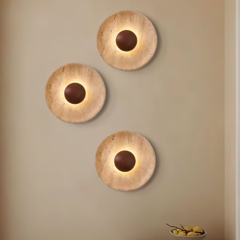 "Three modern, circular wall lamps made of yellow travertine with walnut wood centers, arranged vertically on a wall, providing a warm, ambient glow in a contemporary space."