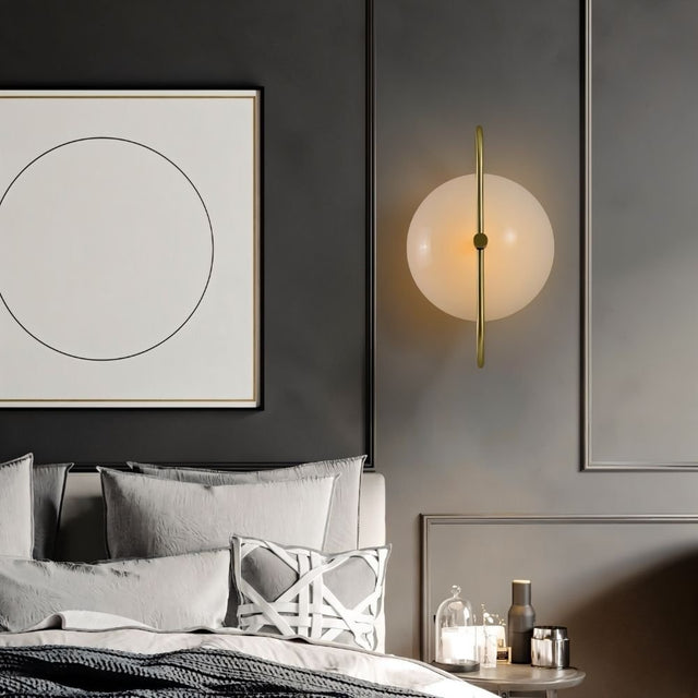 "Brass wall lamp with frosted glass globe in a minimalist bedroom setting, providing a soft, ambient glow."
