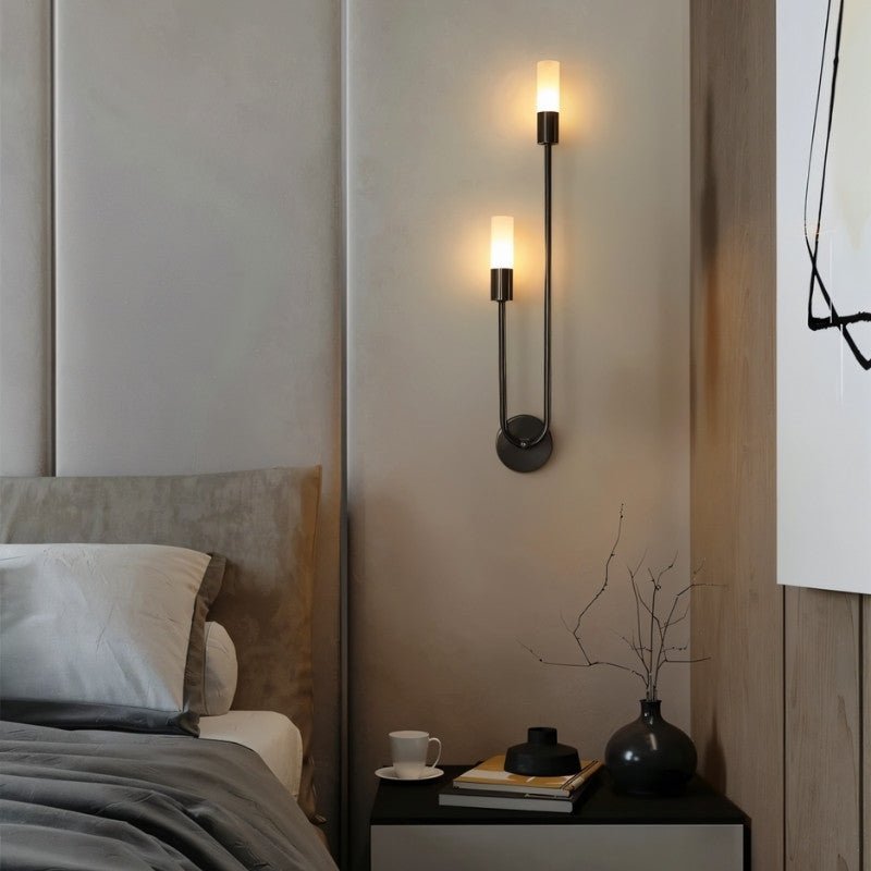 "A modern black wall lamp with two acrylic diffusers on a textured wall in a bedroom."