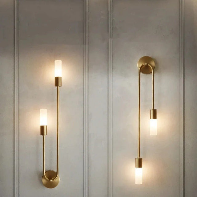"A pair of modern brass wall lamps with acrylic diffusers on a textured wall."