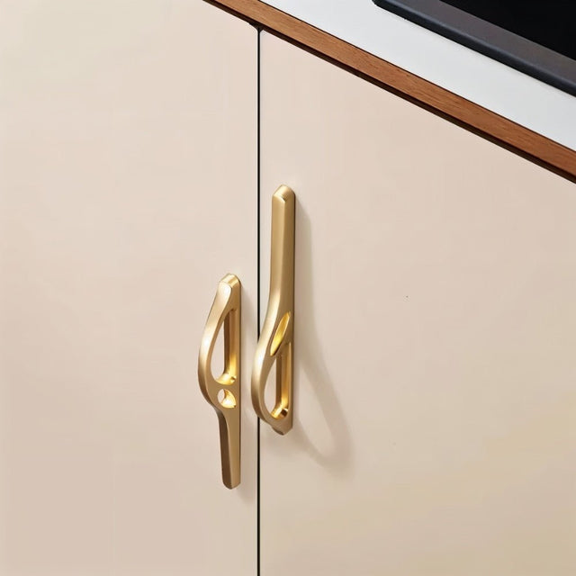 "Two gold zinc alloy pull bars with flowing curves on a light cabinet door."