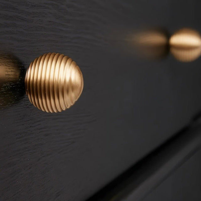 "Gold brass ribbed knob on a dark wooden cabinet."