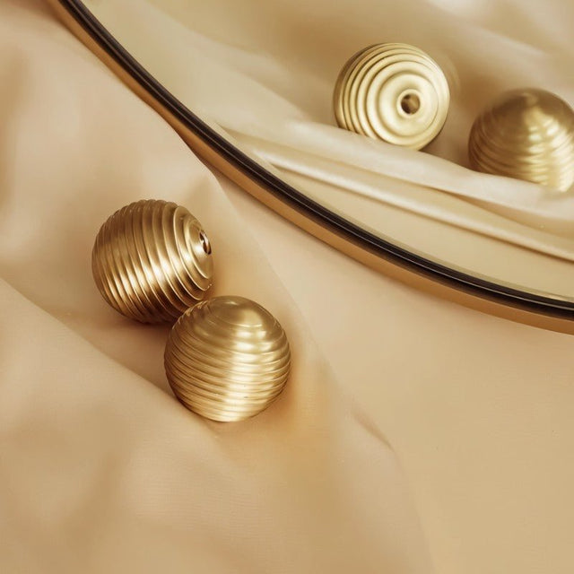 "Set of gold brass ribbed knobs on a cream fabric with a gold-trimmed mirror."
