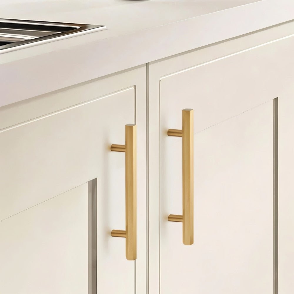 "Modern brass rectangular pull bar handles with cylindrical mounts on white shaker kitchen cabinets."