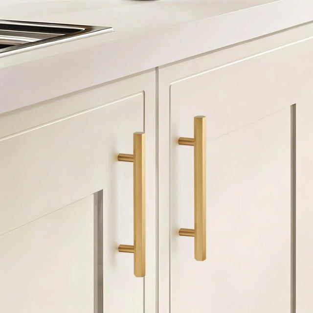 "Modern brass rectangular pull bar handles with cylindrical mounts on white shaker kitchen cabinets."