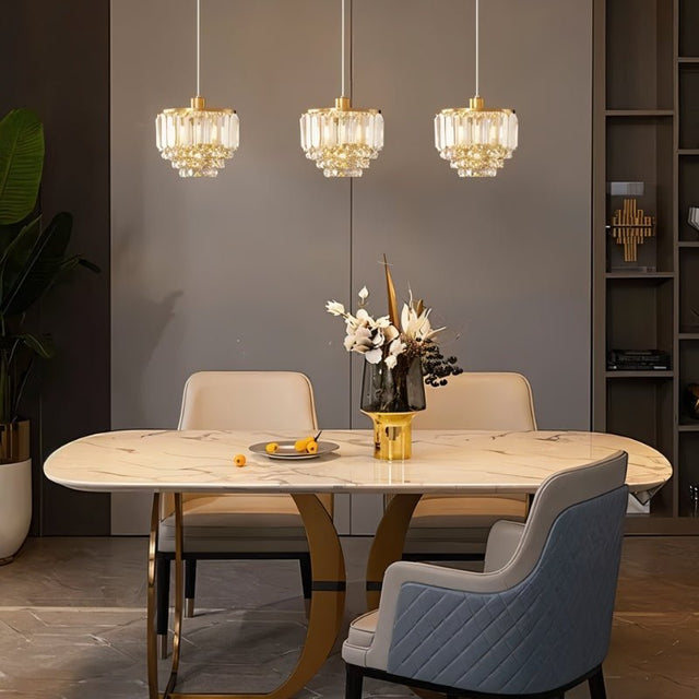 "Three tiered crystal pendant lights with brass frames, hanging above a dining table."