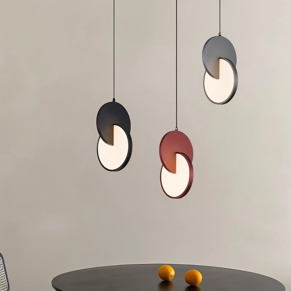 "Modern pendant lights with overlapping discs in various colors above a dining table."