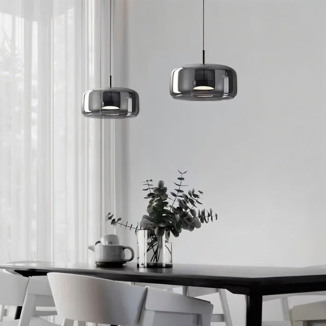 "Two modern pendant lights with smoked glass shades hanging over a dining table."