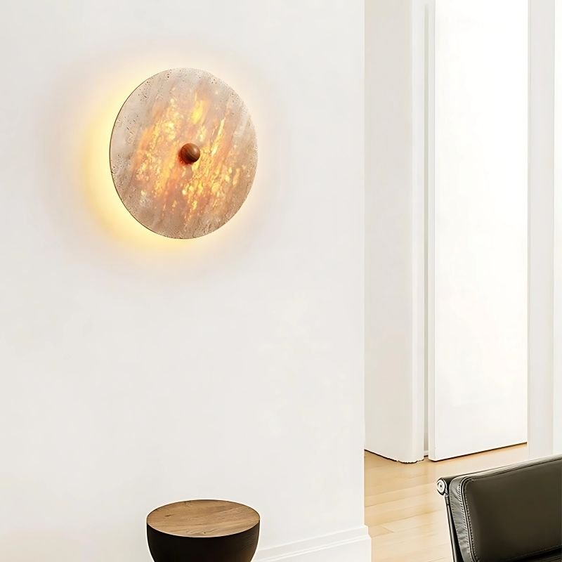 "The Illura Wall Lamp mounted on a wall, showcasing its circular design made of travertine stone and the warm, diffused lighting effect."