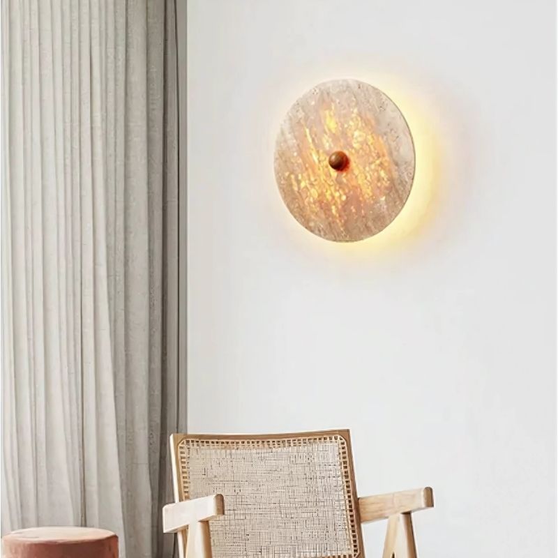 "The Illura Wall Lamp in a bedroom, creating an elegant and soft lighting ambiance, made of travertine stone with a natural texture."