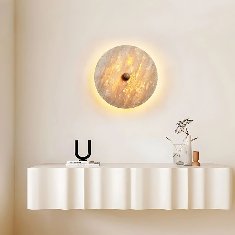 "The Illura Wall Lamp in a living room setting, crafted from travertine stone, casting a soft, organic glow on the wall, enhancing the minimalist decor."