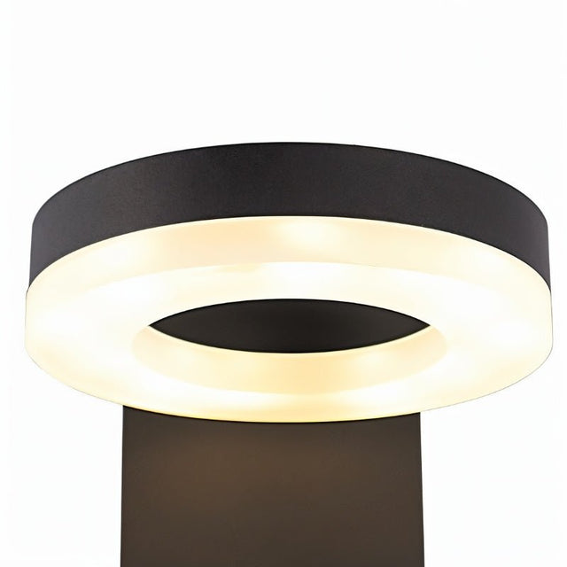 "A close-up of the illuminated LED panel of a black wall lamp with a circular design."