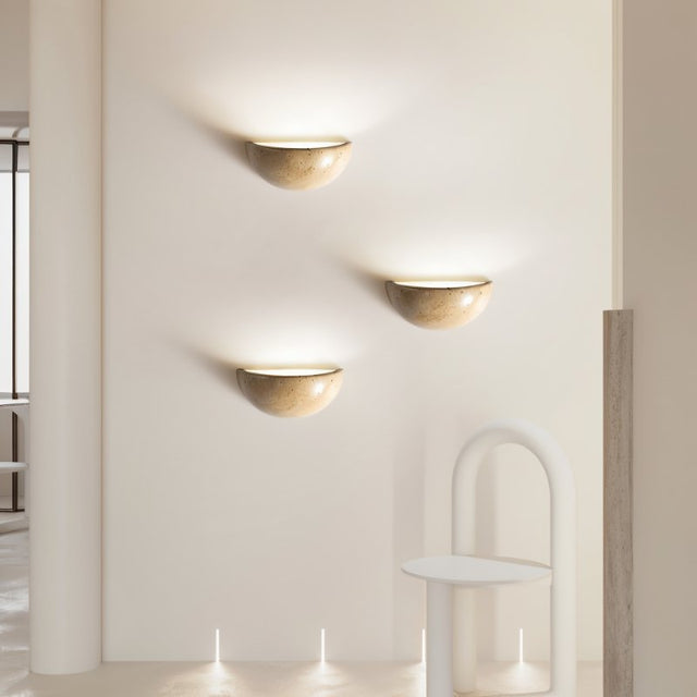 "Three modern, semi-circular wall lamps made of yellow travertine, arranged vertically on a wall, providing soft, ambient lighting."