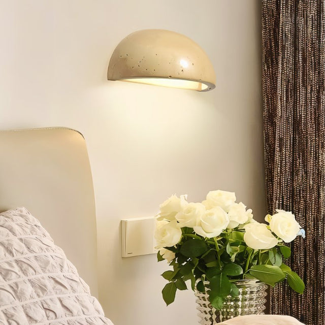 "A modern, semi-circular wall lamp made of yellow travertine, mounted on a wall beside a bed, casting a warm, inviting glow in a bedroom."