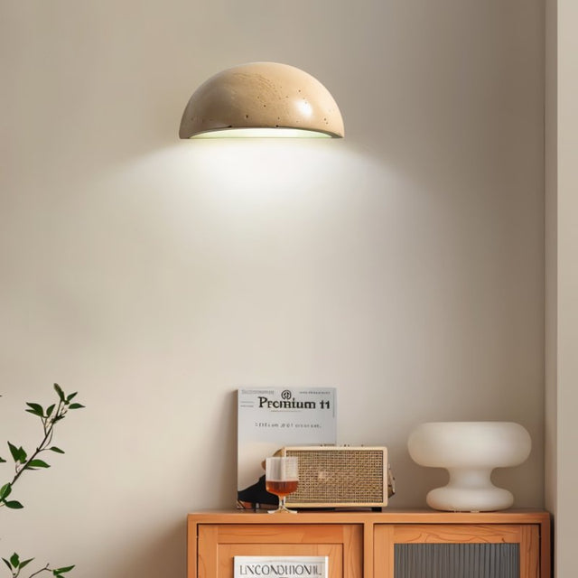 "A modern, semi-circular wall lamp made of yellow travertine, mounted on a wall above a cabinet in a living room, providing a warm, ambient glow."
