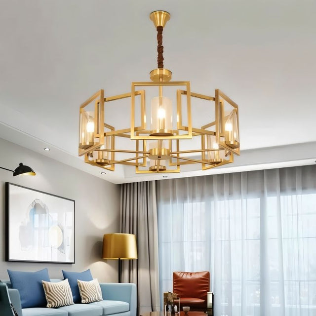 "A modern chandelier with a geometric brass frame and cylindrical glass shades, hanging in a living room with a sofa, curtains, and artwork."