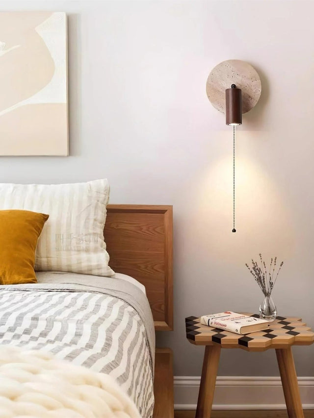 "Yellow travertine round wall lamp with wooden cylindrical shade and pull chain in a bedroom scene, modern bedside light."