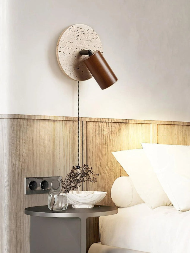 "Yellow travertine round wall lamp with wooden cylindrical shade and pull chain above a bedside table, modern reading light."