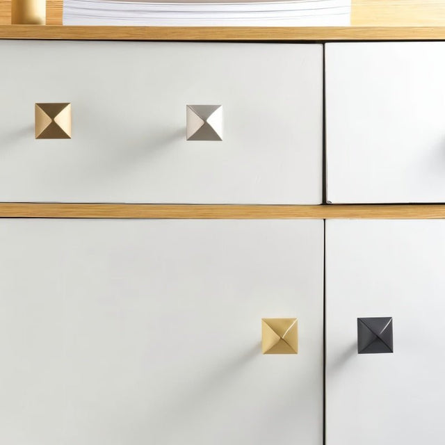 "Pyramid-shaped brass knobs on a white and wood cabinet."