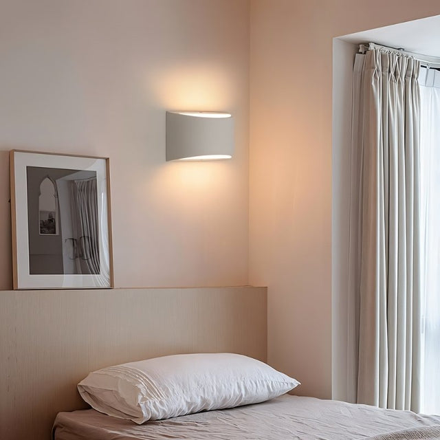 "Modern curved rectangular gypsum wall lamp providing soft ambient light in a contemporary bedroom with a window and sheer curtains."