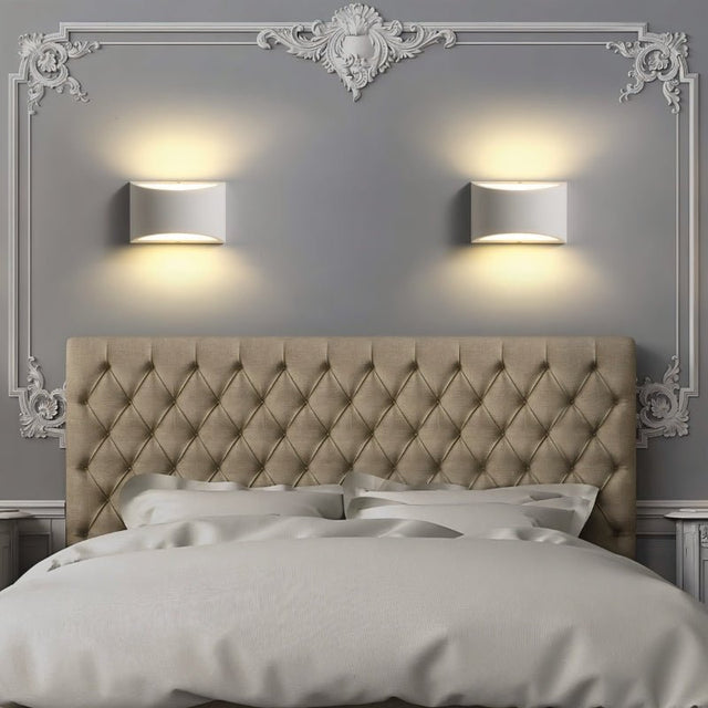 "Pair of modern curved rectangular gypsum wall lamps symmetrically placed above a tufted headboard in a contemporary bedroom, casting soft ambient light."
