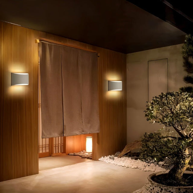 "Pair of modern curved rectangular gypsum wall lamps providing soft ambient lighting in a Japanese-inspired indoor garden setting."