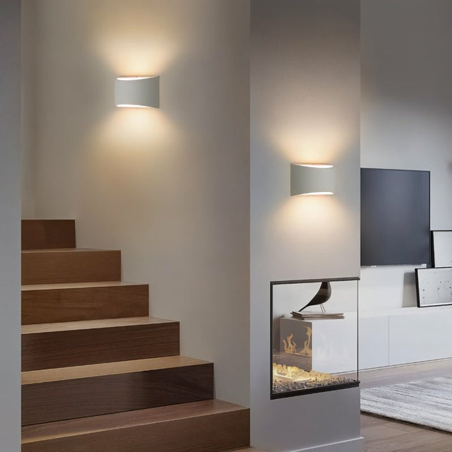 "Pair of modern curved rectangular gypsum wall lamps providing ambient up and down lighting in a contemporary living room with a staircase."