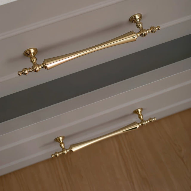 "Brass pull bar handles with a tapered spindle design and intricate finials on light grey drawers."
