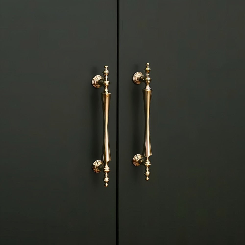 "Pair of brass handles with a tapered spindle design and intricate finials on a dark-colored cabinet."