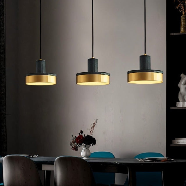 "Three modern pendant lights with black marble and brass accents hang over a dining table, creating a warm and stylish ambiance."