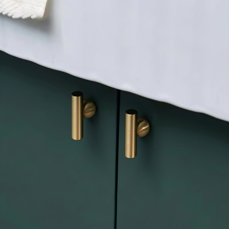 "Two gold brass knobs with cylindrical design, mounted on dark green cabinet doors."