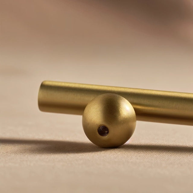 "Close-up of a gold brass knob and pull bar showing the screw hole in the knob, resting on a brown surface."