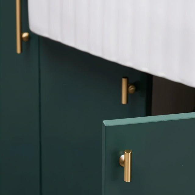 "Gold brass knobs with cylindrical design, mounted on dark green kitchen cabinet doors, with one door slightly ajar."