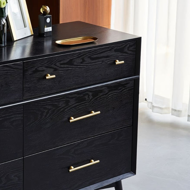 "Gold brass knobs and pull bars with cylindrical design, mounted on a black wooden dresser with drawers."