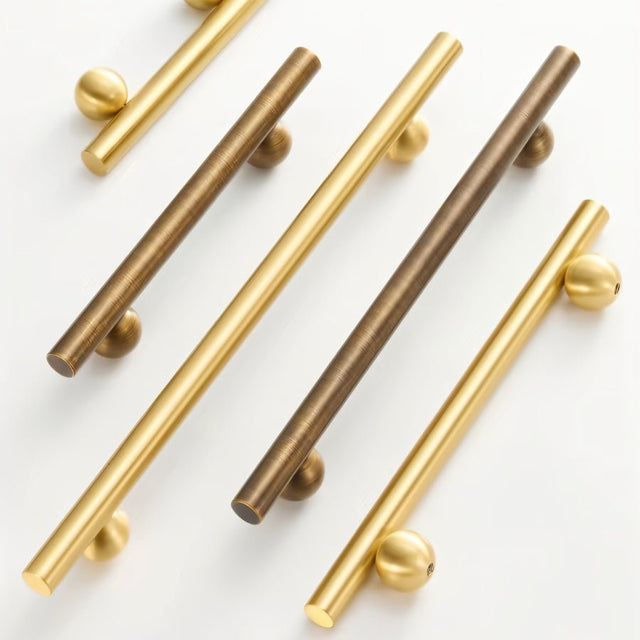 "Set of gold and bronze brass knobs and pull bars with cylindrical design, arranged diagonally on a white background."