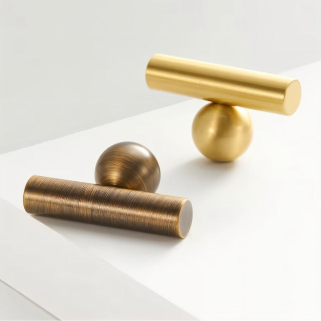 "Gold and bronze brass knob and pull bar with cylindrical design, resting on a white surface."