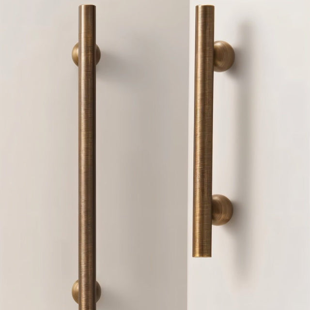 "Two bronze brass pull bars with cylindrical design and textured finish, mounted vertically on white cabinet doors."