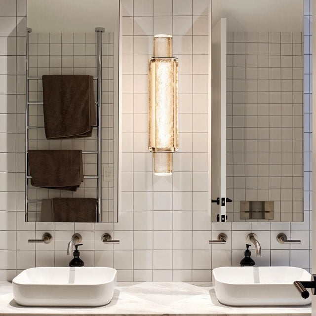 "Modern crystal wall lamp with a vertical, cylindrical design, mounted on a wall in a contemporary bathroom."