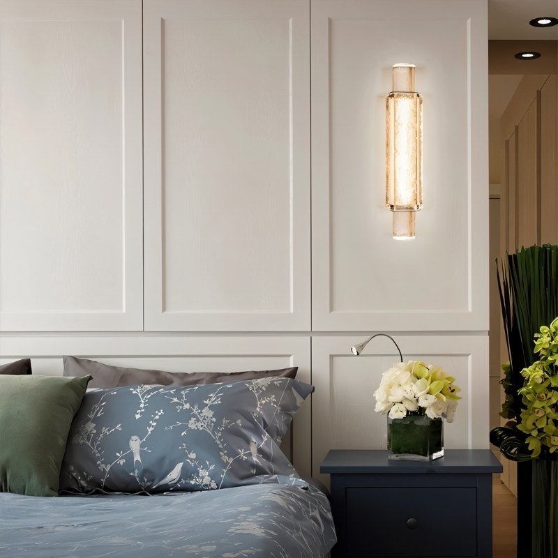 "Modern crystal wall lamp with a vertical, cylindrical design, providing soft lighting in a contemporary bedroom."
