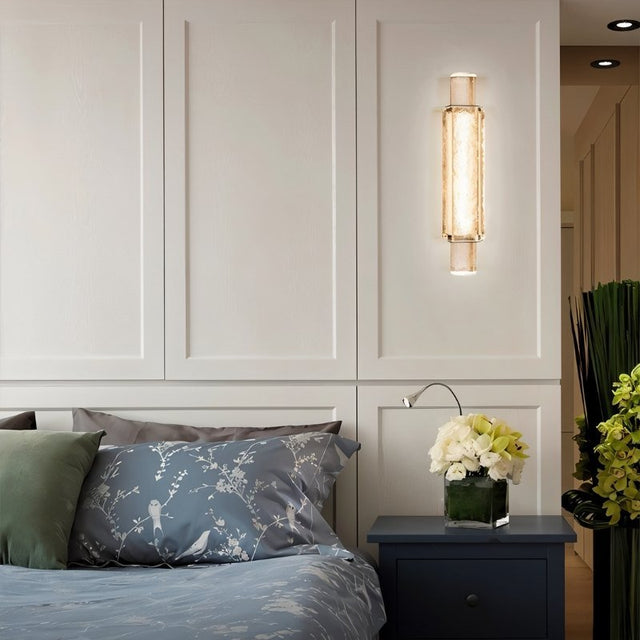 "Modern crystal wall lamp with a vertical, cylindrical design, providing soft lighting in a contemporary bedroom."