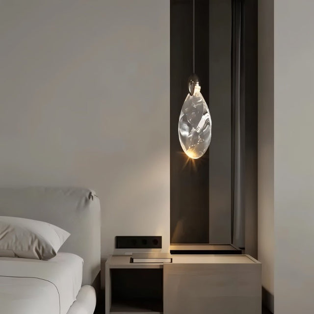 "A single, uniquely shaped crystal pendant light hangs next to a bed in a modern bedroom, casting a warm, ambient glow."
