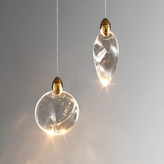 "Close-up of two uniquely shaped crystal pendant lights with gold accents, showcasing their elegant design and warm glow."