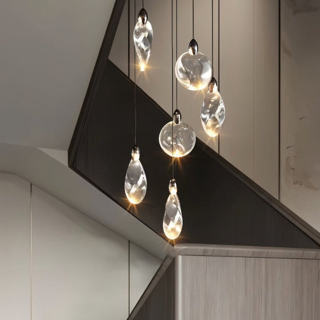 "A cluster of uniquely shaped crystal pendant lights hang above a modern staircase, creating a cascading effect of warm light."