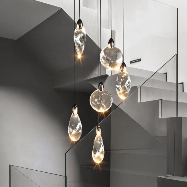 "Pendant lights with uniquely shaped crystal droplets hang from a black canopy, creating a cascading effect down a modern staircase."