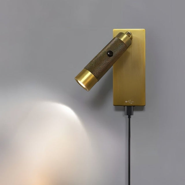"Close-up of a modern, cylindrical bedside reading lamp with a textured polished metal finish, wall-mounted with an adjustable light direction and USB connection."