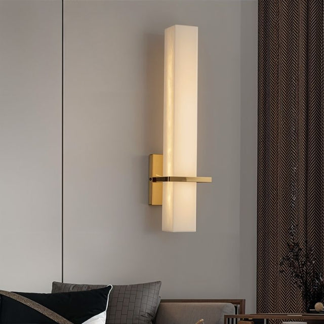 "Modern wall lamp with an alabaster cylindrical shade and brass accents, mounted in a bedroom, providing soft ambient lighting"