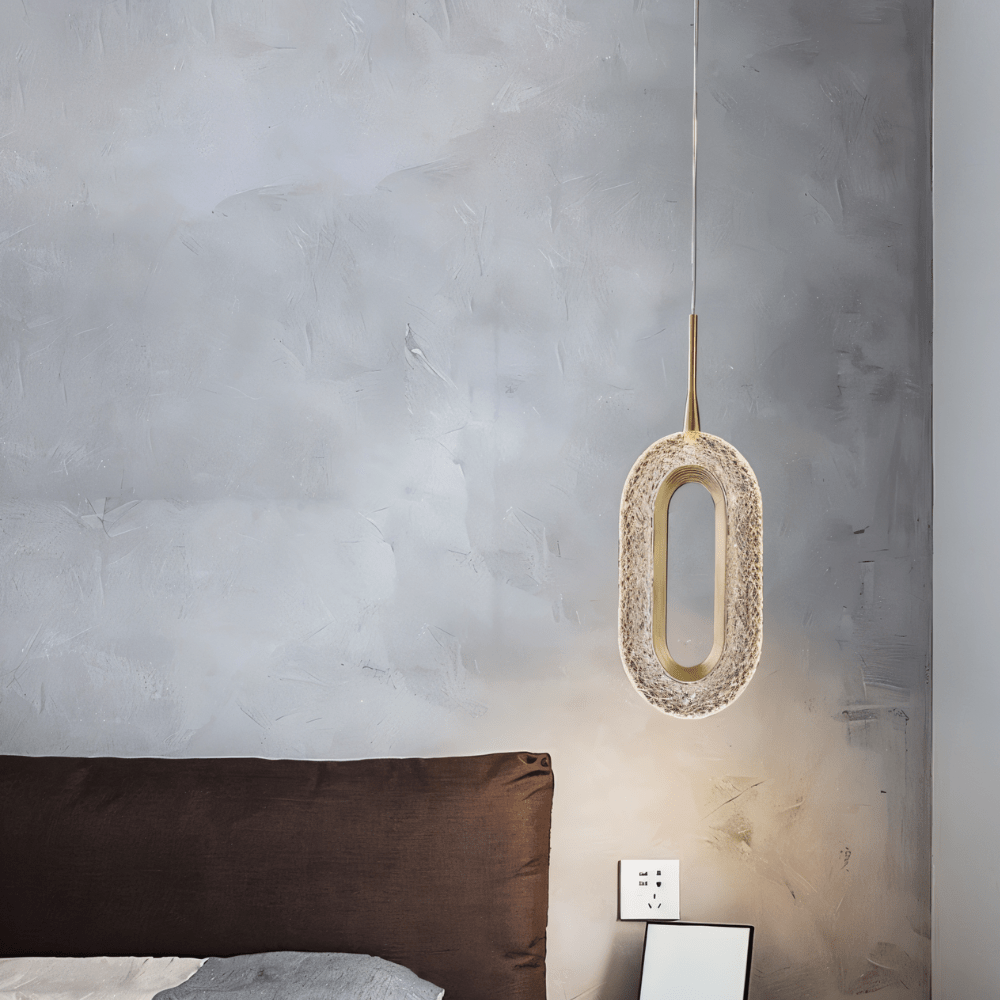 Single Luxin Pendant Light with sculptural oval LED design, hanging beside a brown bed in a minimalist bedroom with textured wall.