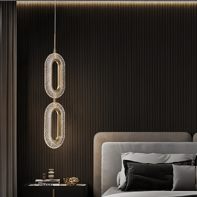 Double Luxin Pendant Light in copper and acrylic, casting soft ambient glow in a dark-toned modern bedroom with vertical paneling.