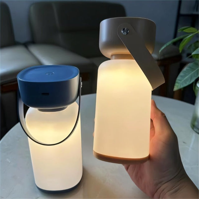 "Two cylindrical table lamps with handles, one in blue and white, the other in beige and white, being held by a hand."